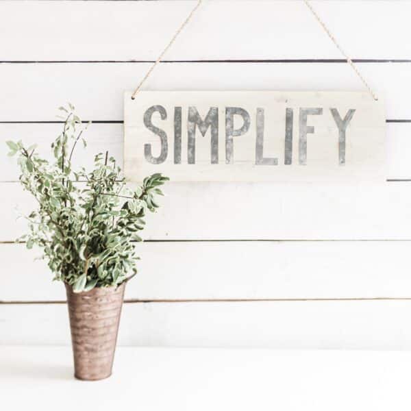 A green plant sitting on a table with a sign hanging behind it that says "simplify".